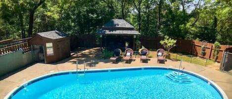 Ein Pool mit Liegestühlen und einer Laube in einer schattigen, von Bäumen umgebenen Zone.