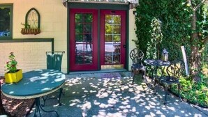 Un patio con una puerta roja, un toldo verde y mobiliario exterior.