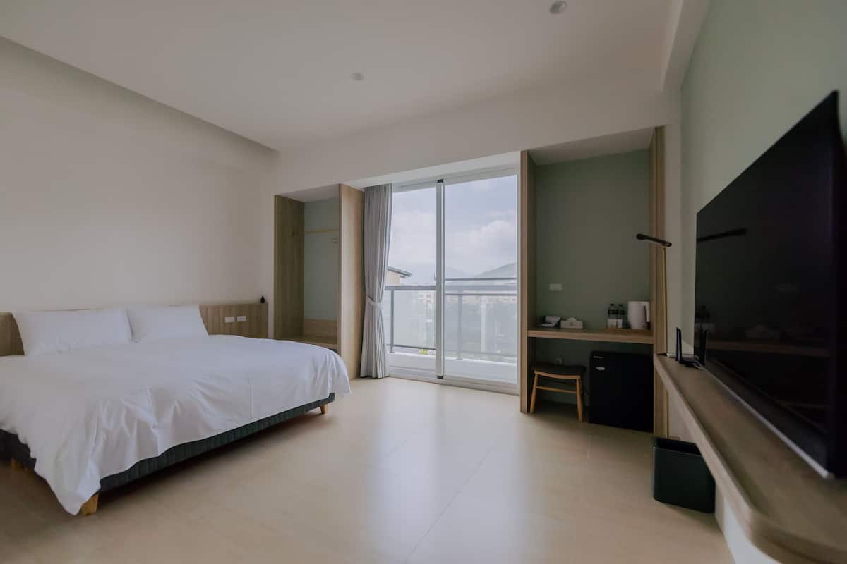 A hotel room with a large bed, a TV, a small desk, and a balcony with a view.