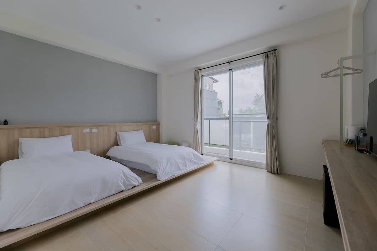 A hotel room with a large bed, a wooden headboard, a sliding glass door to the balcony, and a wooden desk with a mirror.