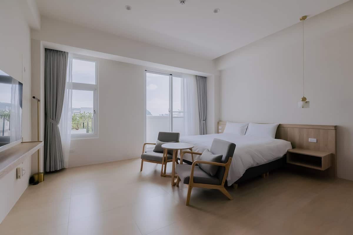 A modern hotel room with a large bed, a small table, two chairs, and a TV.