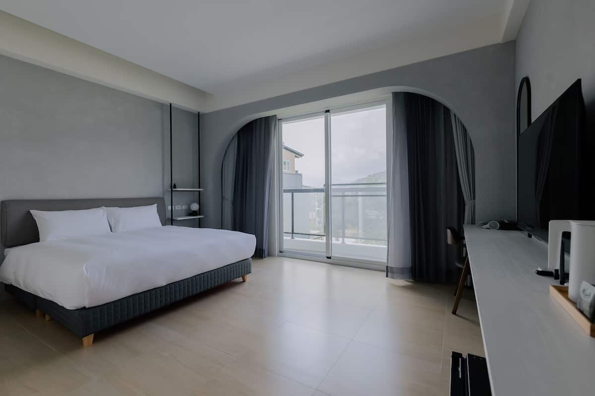 A modern hotel room with a large bed, a desk, and a view of the outside.