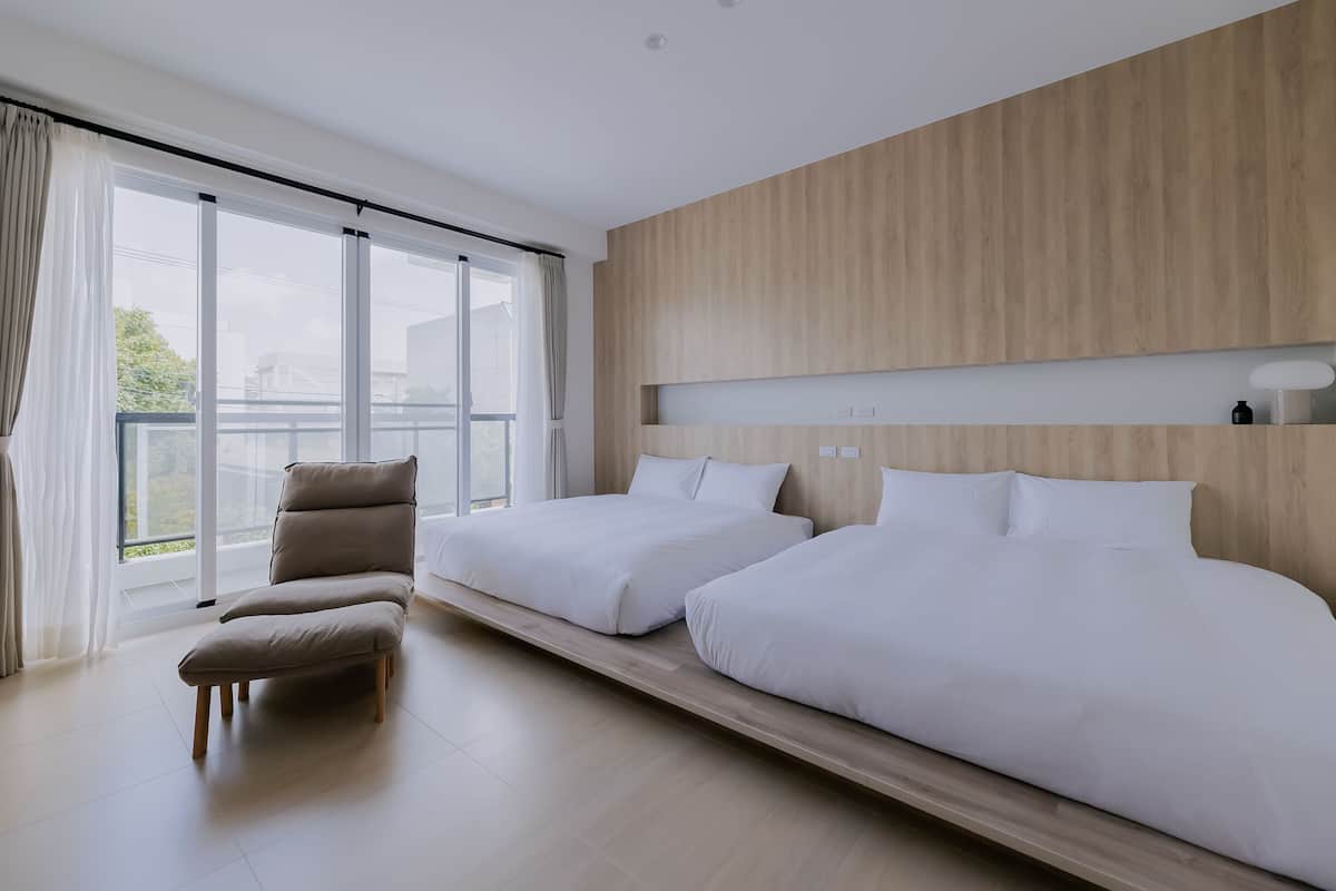 A modern hotel room with two beds, a large window, and a view of the outdoors.
