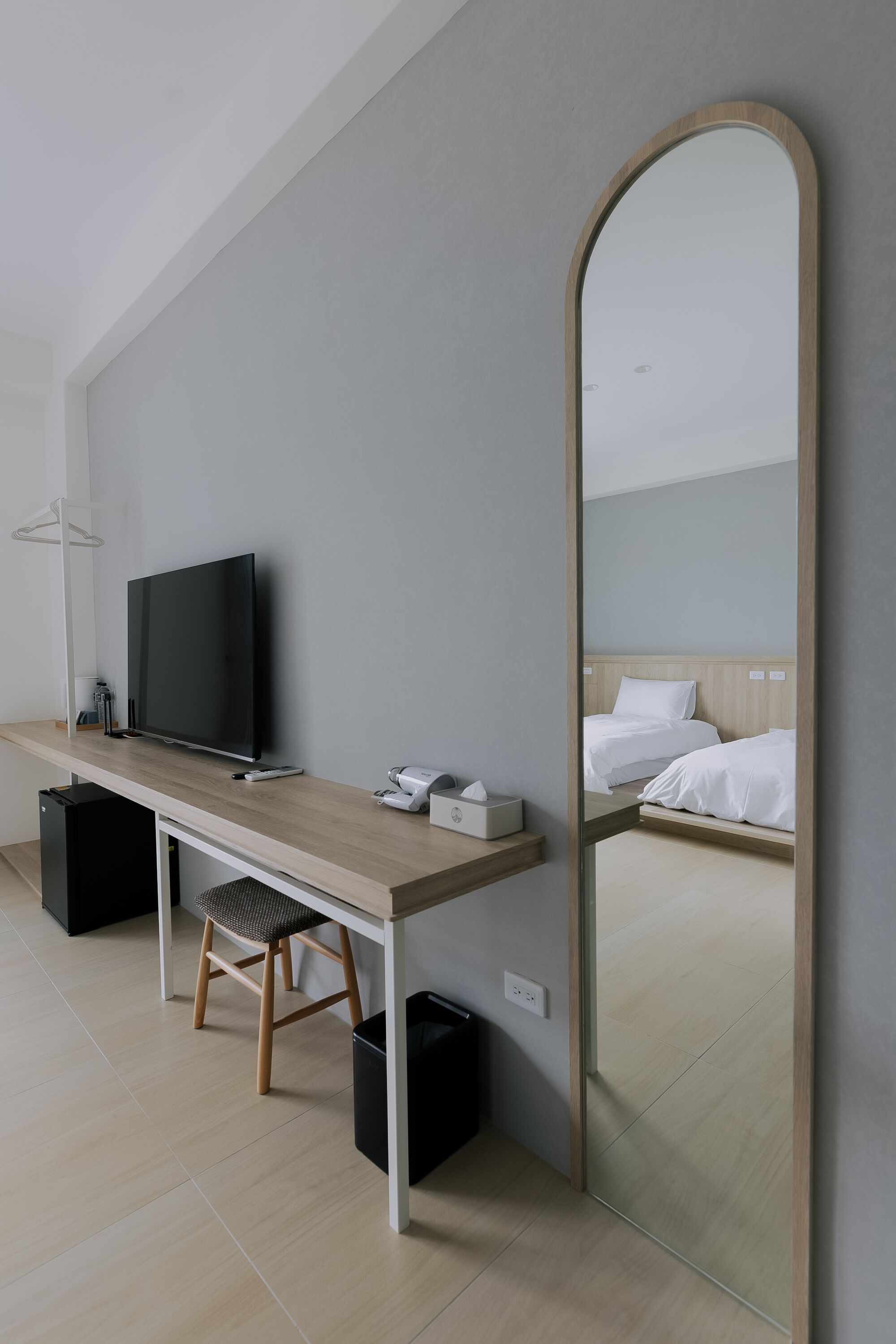 Una habitación de hotel moderna con un escritorio de madera, un televisor de pantalla plana, un espejo y una cama con ropa blanca.