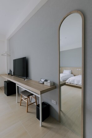 A modern hotel room with a wooden desk, a flat-screen TV, a mirror, and a bed with white linens. - terumahouse (Taitung)