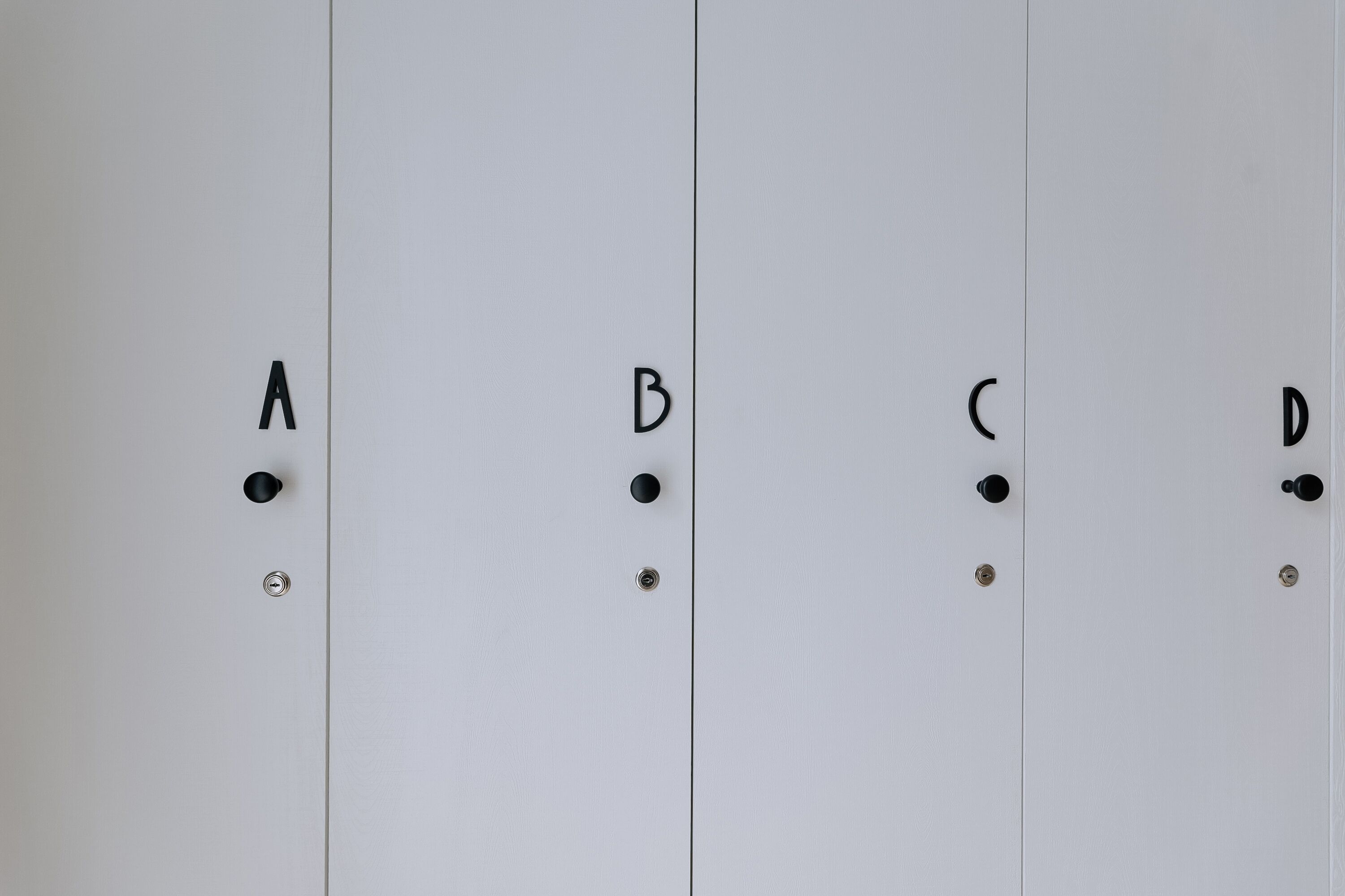 Cuatro taquillas blancas con manijas y tornillos negros, etiquetadas A, B, C y D.
