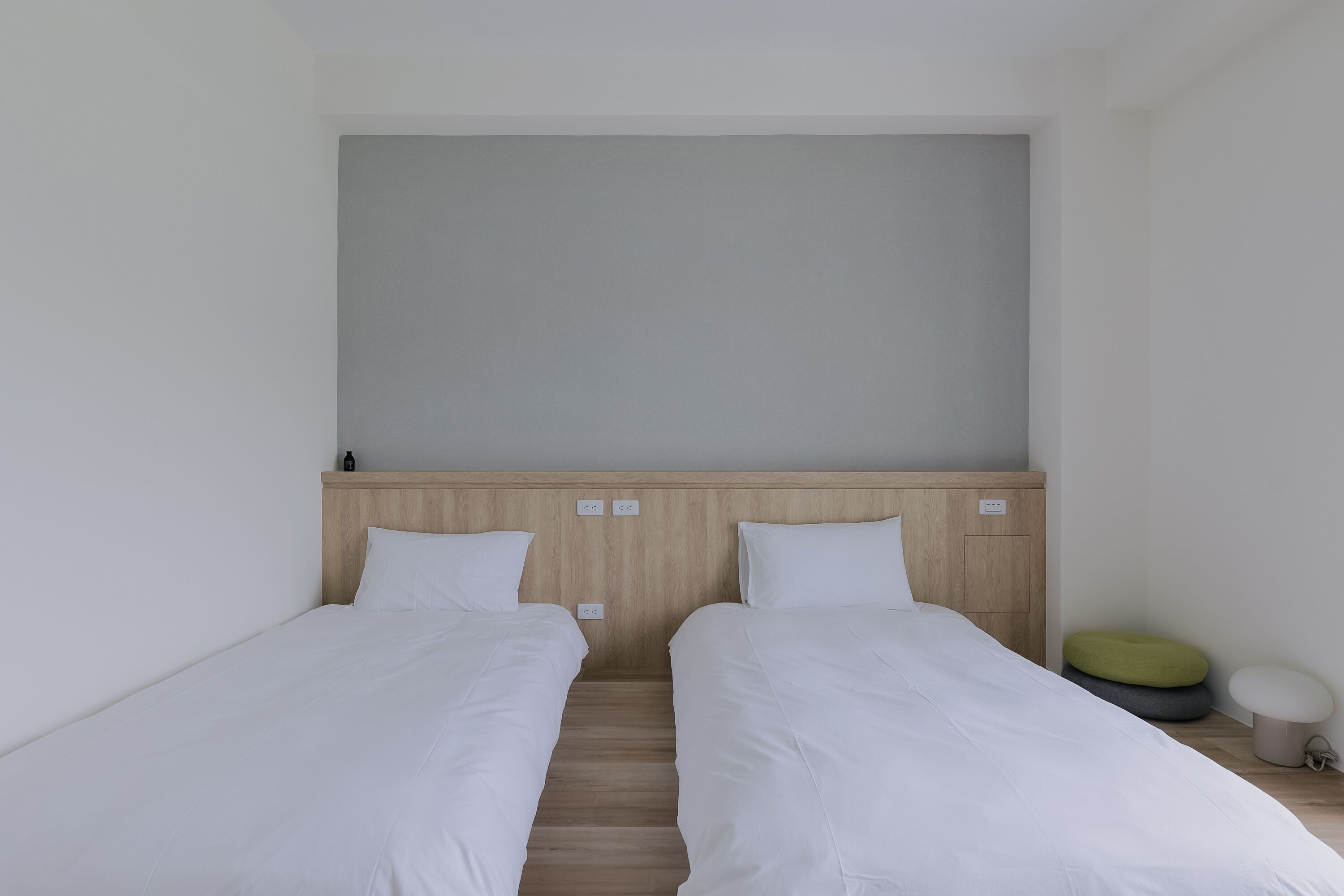 A room with two single beds, a wooden headboard, and a small bedside table with a lamp.