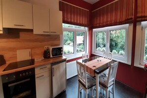 Een compacte keuken met witte kastjes, een magnetron, een vaatwasser en een eettafel met stoelen.