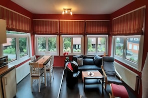 A modern living room with a dining area, large windows with curtains, a sofa, and a coffee table.