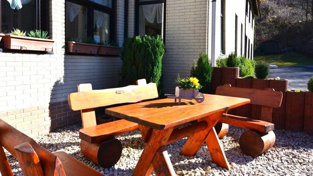 Un espace extérieur aménagé avec des bancs et une table, le tout en bois, entouré de plantes en pot et bordé d’un mur de briques.