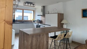 Moderni keittiö, jossa on valkoiset kaapit, puinen keittiösaareke ja punotut baarituolit.