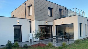 Moderni, kaksikerroksinen talo, jossa on suuret lasi-ikkunat, parveke ja hyvin hoidettu nurmikko.