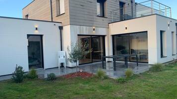 Een modern herenhuis met twee verdiepingen, grote glasramen, een balkon en een verzorgd gazon.