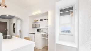 Una cocina compacta con muebles blancos, una cafetera y vistas por una ventana.