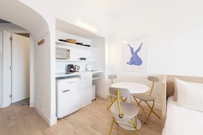 A compact living space with a kitchenette, a dining area with a small table and chairs, and a bed with a headboard.