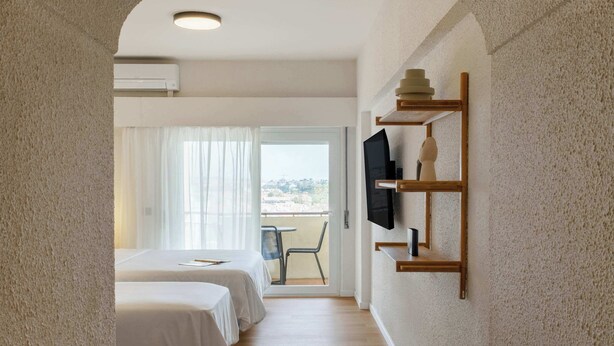 Habitación de hotel con dos camas, un televisor montado en la pared y un balcón con vistas.