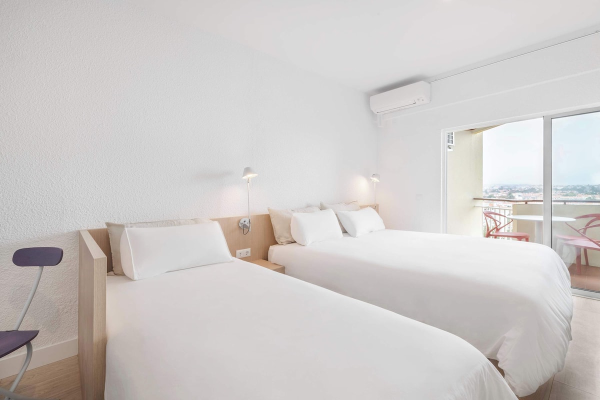 A hotel room with two beds, a balcony with a view, and a chair.