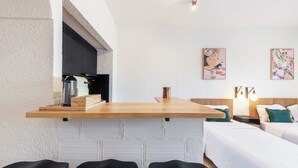 Habitación de hotel pequeña con kitchenette, una cama, zona de estar con sillas y obras de arte en las paredes.