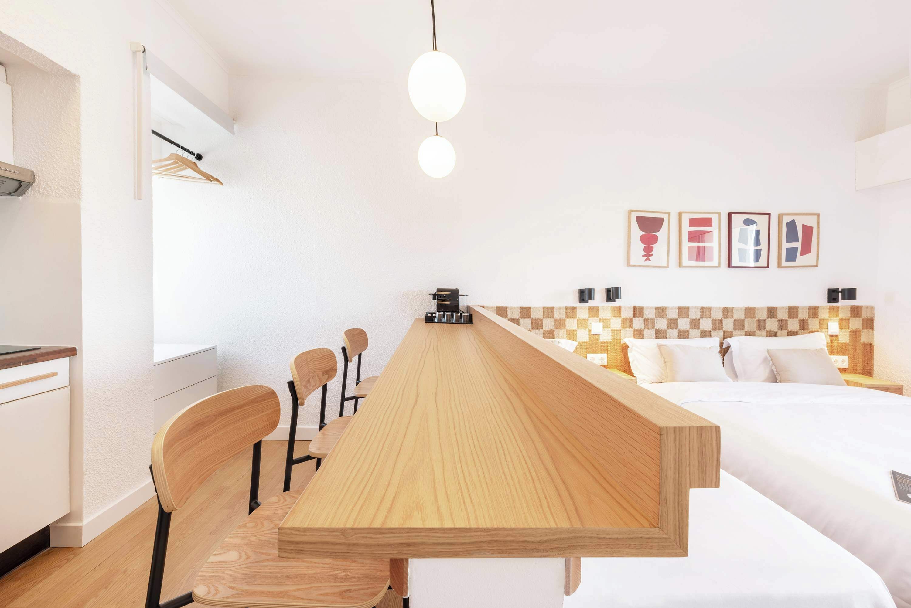 Una habitación de hotel moderna con una mesa de comedor de madera, una cama con cabecero a cuadros y una pequeña kitchenette.