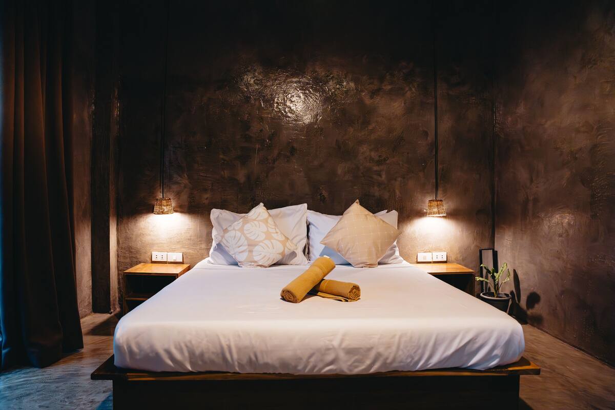 A neatly made bed with white linens, two rolled towels, and patterned pillows. There are two bedside lamps on wooden nightstands.