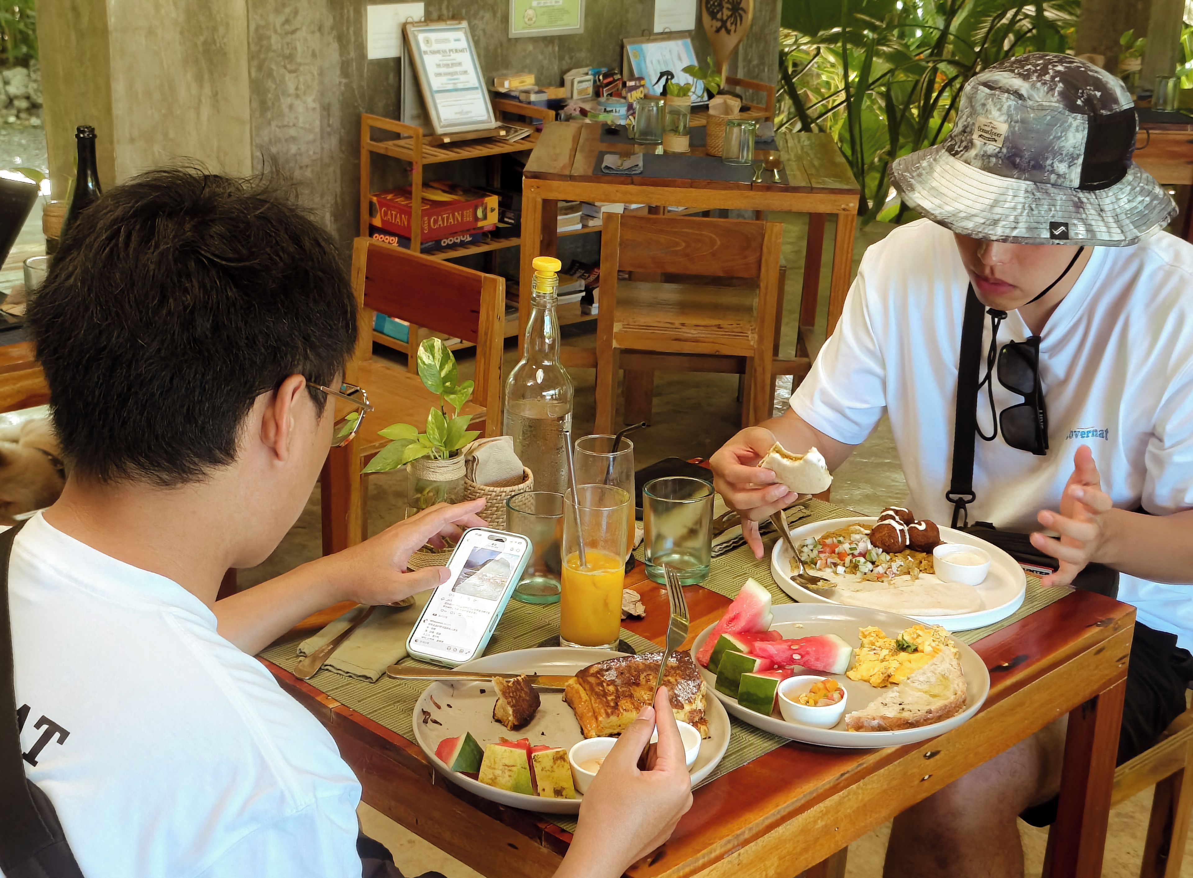 Two people dining at a wooden table with various dishes, a bottle, and a smartphone.