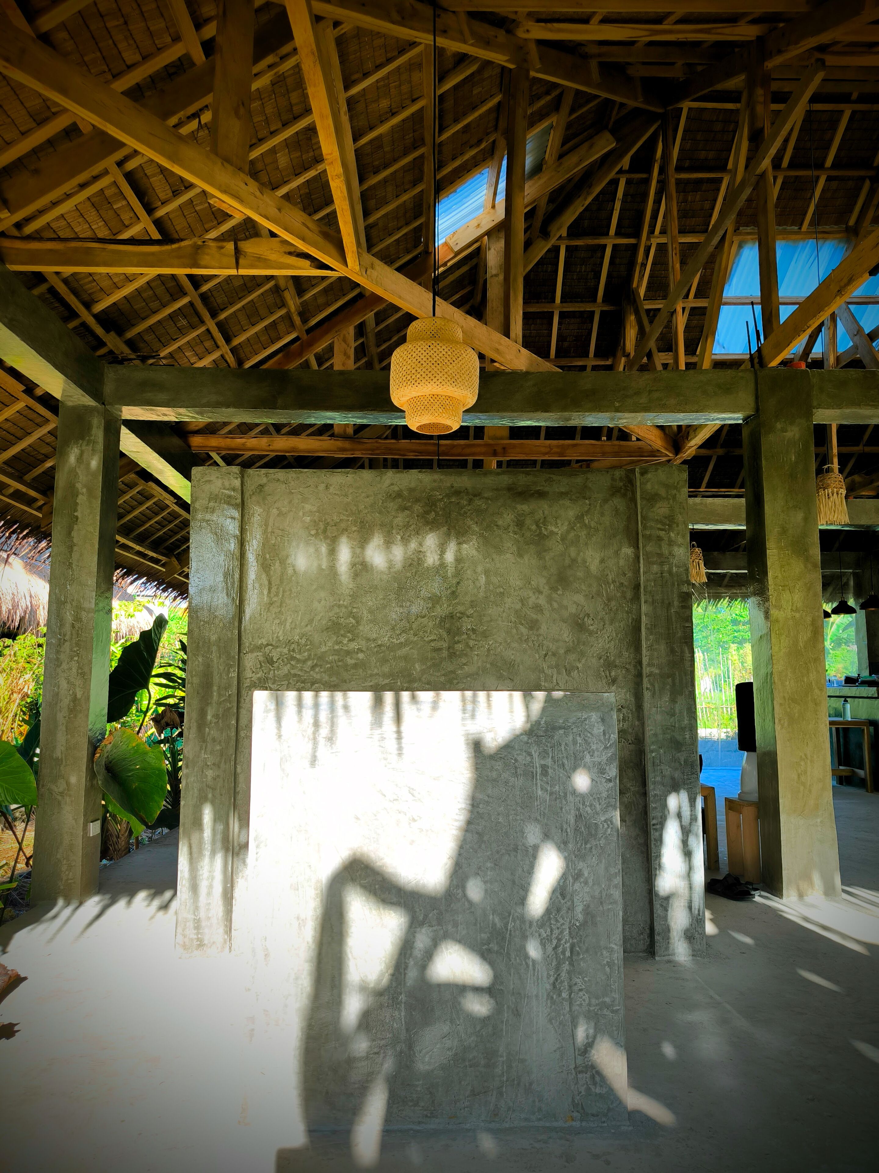 A spacious room with a high ceiling and exposed wooden beams, a hanging light fixture, and a concrete pillar.