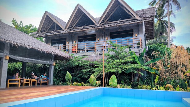 Un resort con piscina, terraza de madera y construcciones de techo de paja.
