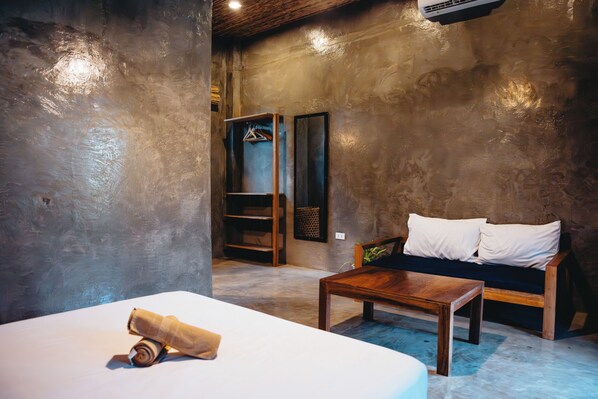 A room with a bed, a wooden table, a sofa with white cushions, and a wardrobe with a hanging rack. - The Ohm Siargao Resort (General Luna)