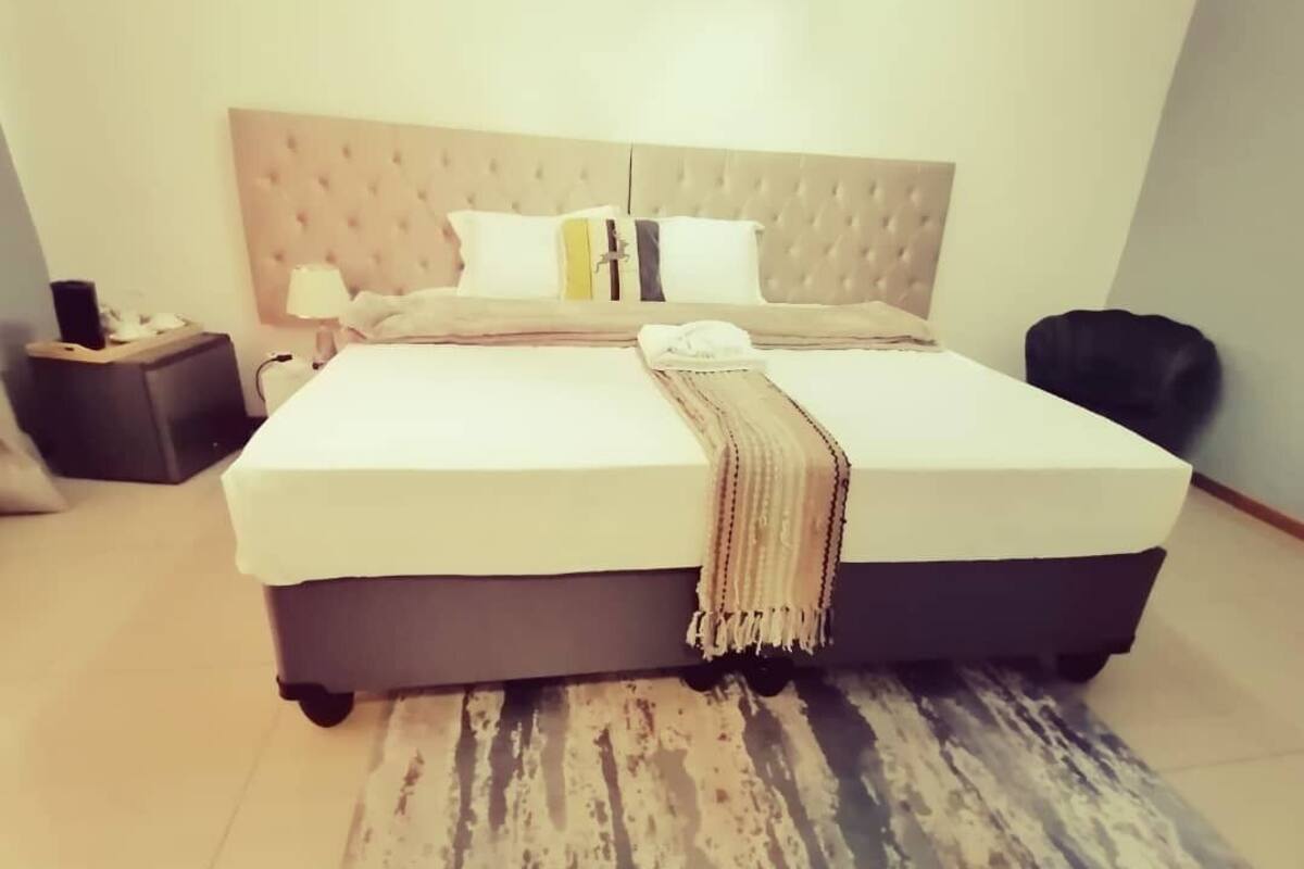 A neatly made bed with a tufted headboard, a bedside table with a lamp, and a small nightstand.