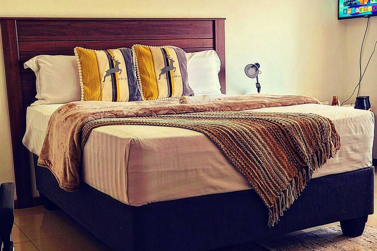 A neatly made bed with a wooden headboard, a patterned throw blanket, and decorative pillows.