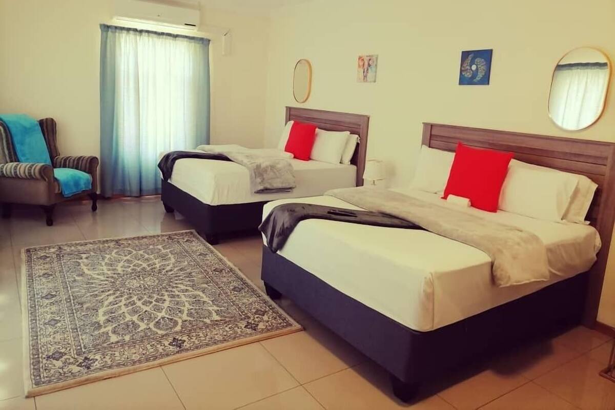 A hotel room with two beds, a chair, a rug, and a window with curtains.