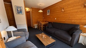 Un salon chaleureux avec un canapé, un fauteuil et une table basse, des murs en bois et un coin repas avec des chaises.
