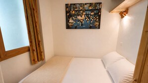 Un lit simple avec une tête de lit, une fenêtre avec des rideaux et une œuvre d’art accrochée au mur.
