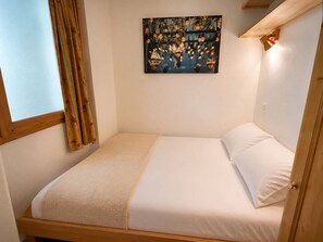 A single bed with a headboard, a window with curtains, and a wall-mounted artwork.