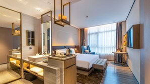 Ett modernt hotellrum med en stor säng, ett separat badrum med handfat, en sittgrupp och en tv som är monterad på väggen.
