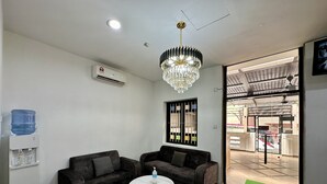 Una habitación moderna con dos sofás oscuros, una mesa redonda blanca, un dispensador de agua y un ventanal con vistas al exterior.