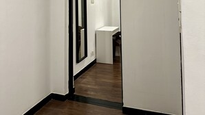 Un pasillo estrecho con paredes blancas y suelo de madera. Al final hay una puerta que da a un baño con lavamanos y espejo blancos.