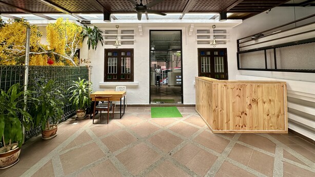 Un espacio interior con mostrador de recepción de madera, una zona de estar con mesa y sillas, y un techo con diseño de cuadrícula.
