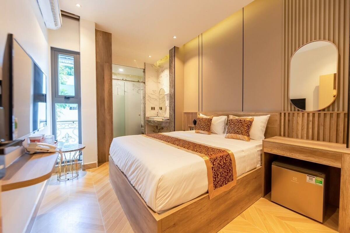 Een moderne hotelkamer met een groot bed, een klein bureau, een spiegel en een compacte kitchenette.
