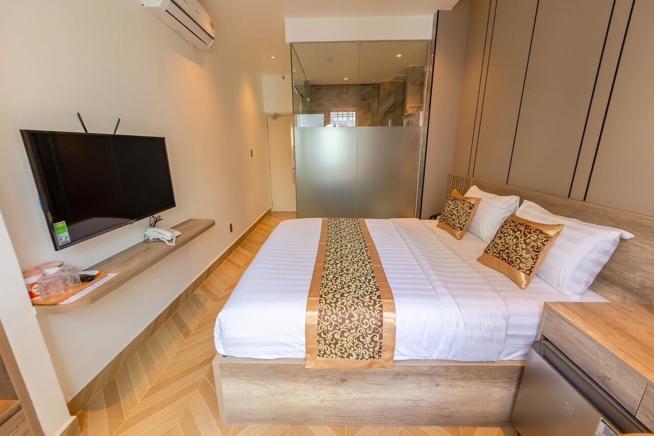 A hotel room with a large bed, a TV on a stand, a wooden floor, and a glass partition.