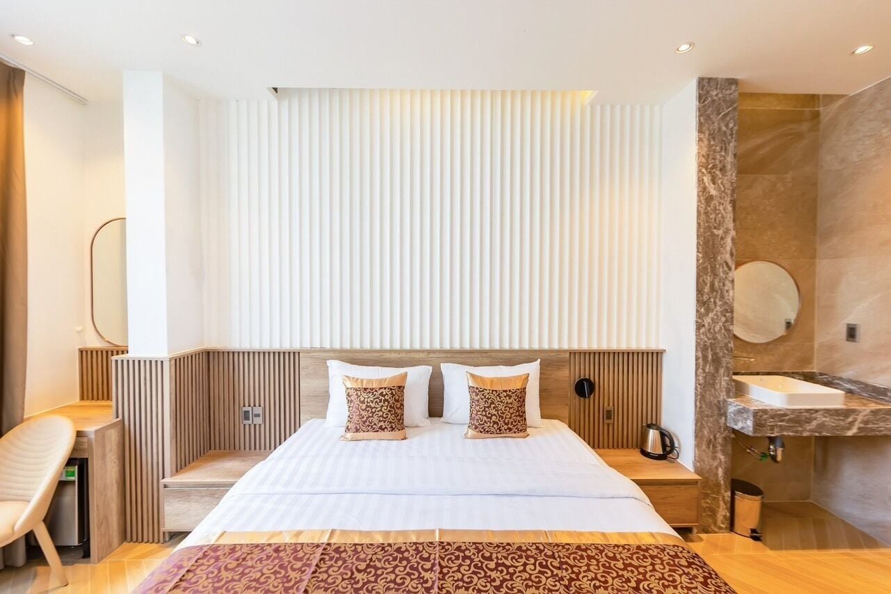 A modern hotel room with a large bed, a wooden headboard, a bedside table with a lamp, and a bathroom with a marble countertop.