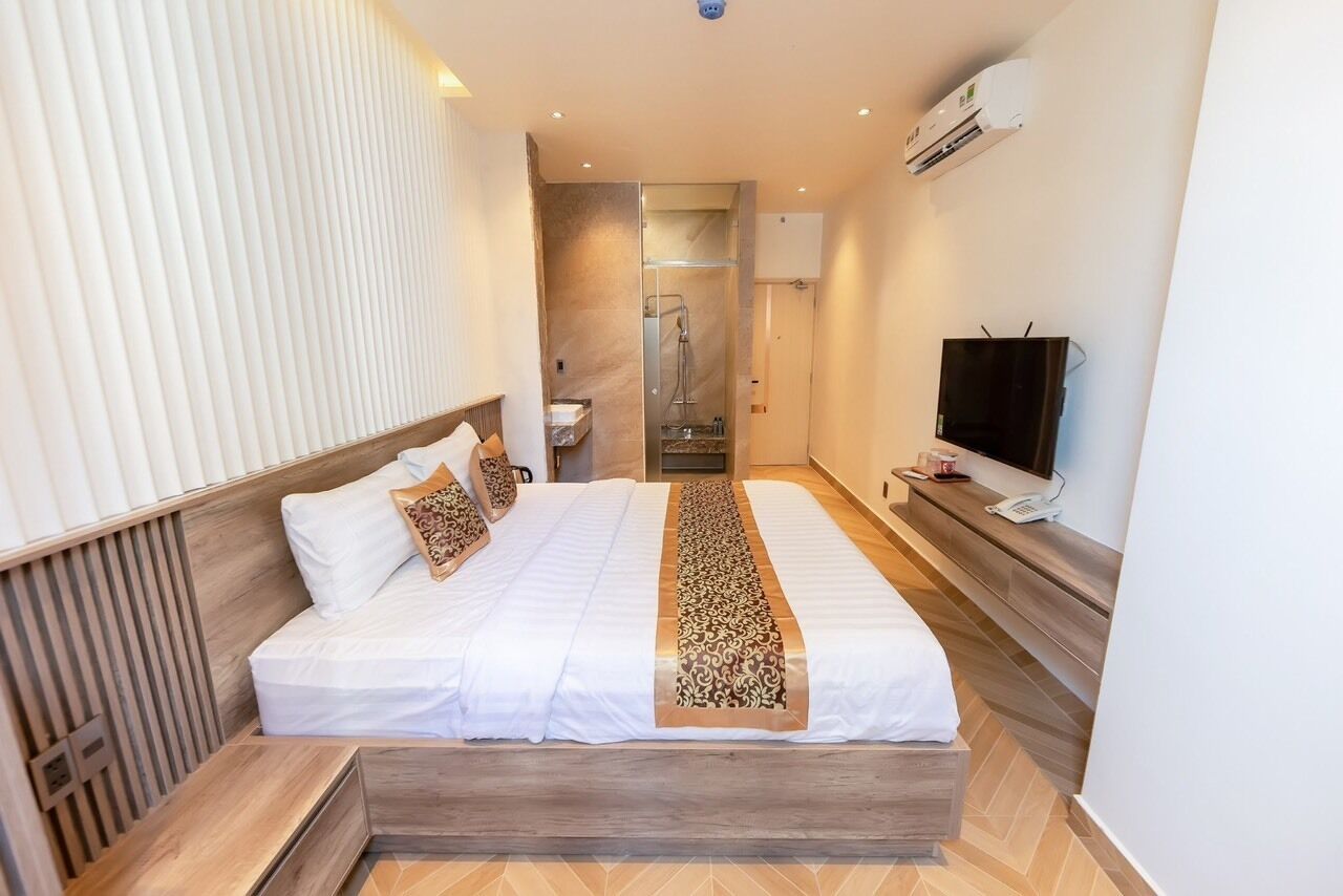 A hotel room with a large bed, a TV, and an air conditioning unit.