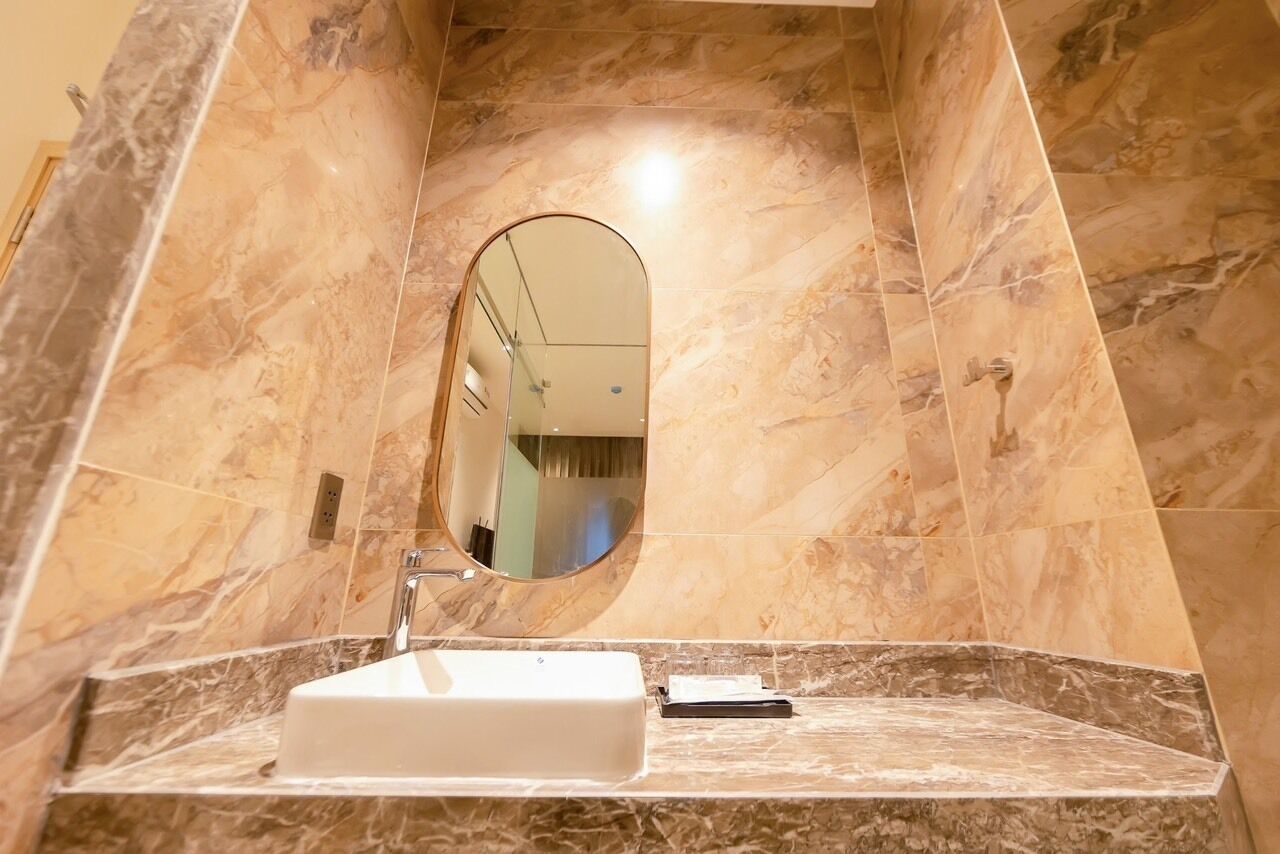 Un baño con un lavamanos de mármol, un espejo y un dispositivo portátil sobre la encimera.