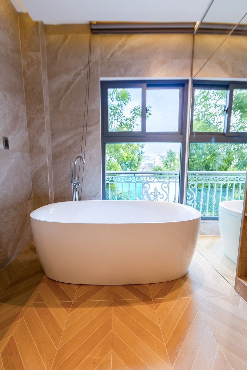 Un baño moderno con una bañera independiente, un cabezal de ducha y vistas a un balcón con vegetación.