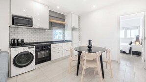 Een moderne keuken met witte kasten, een inbouwoven, een wasmachine en een eetgedeelte met een ronde tafel en stoelen.