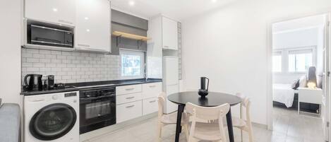 Een moderne keuken met witte kasten, een inbouwoven, een wasmachine en een eetgedeelte met een ronde tafel en stoelen.