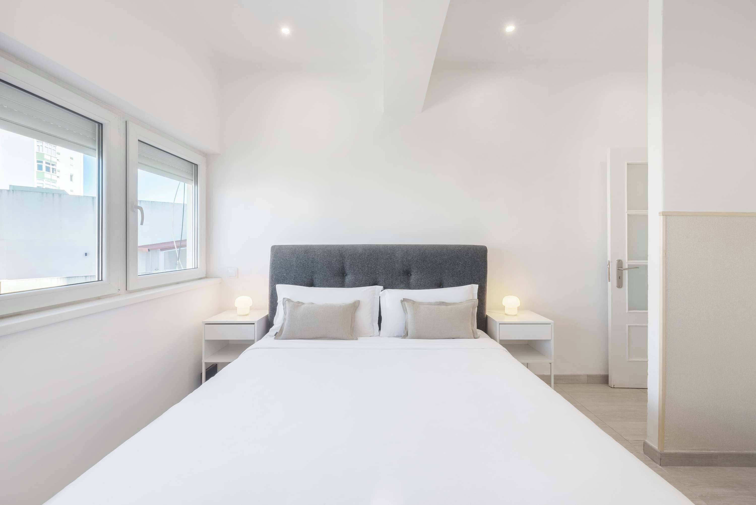 Un dormitorio moderno con una cama grande, dos mesitas de noche y un ventanal.