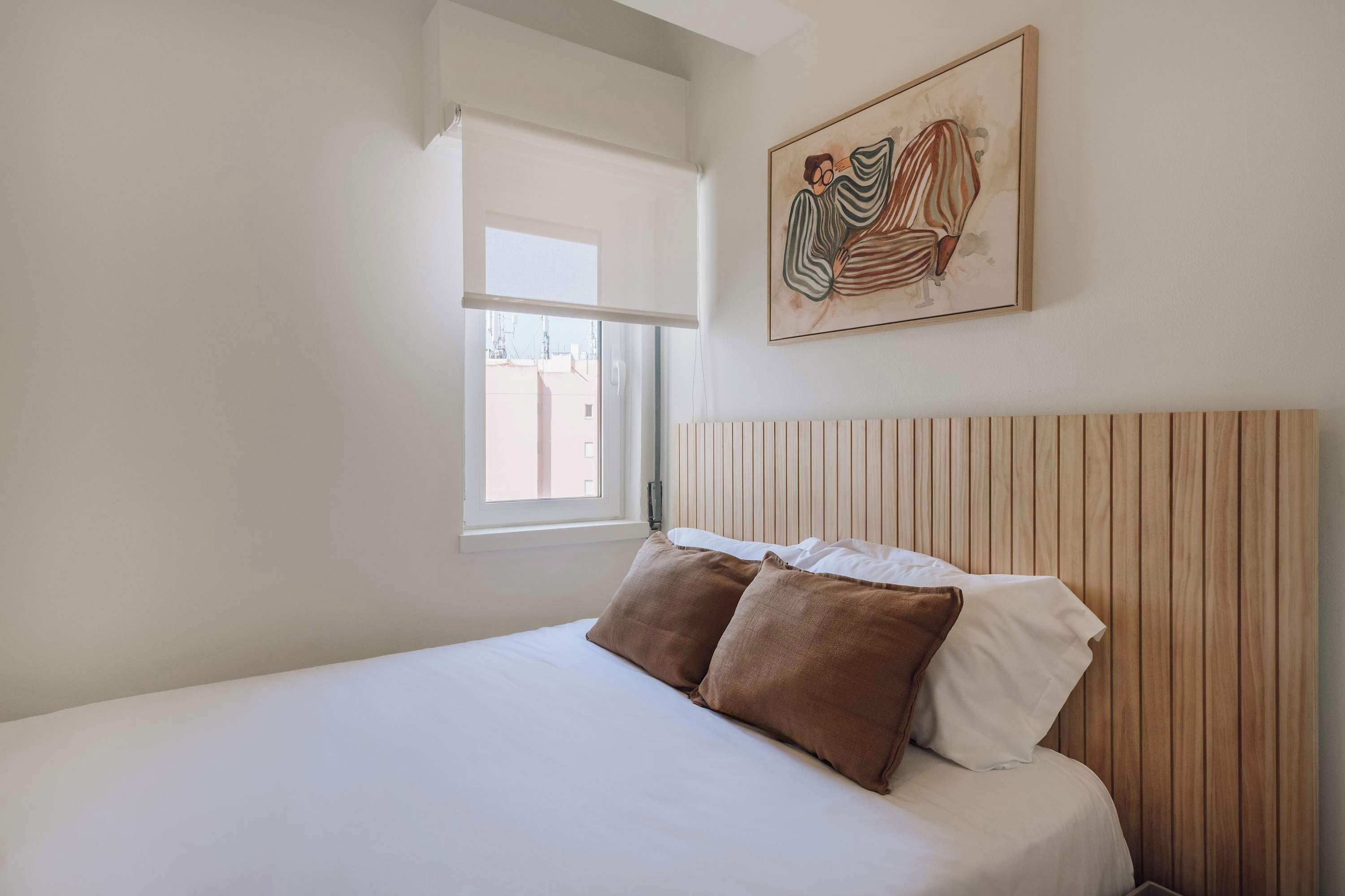 Een slaapkamer met een bed, een raam en een schilderij dat aan de muur hangt.