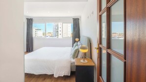 Een moderne hotelkamer met een groot bed, een bedlamp, een nachtkastje van hout en uitzicht op de stad door grote ramen.