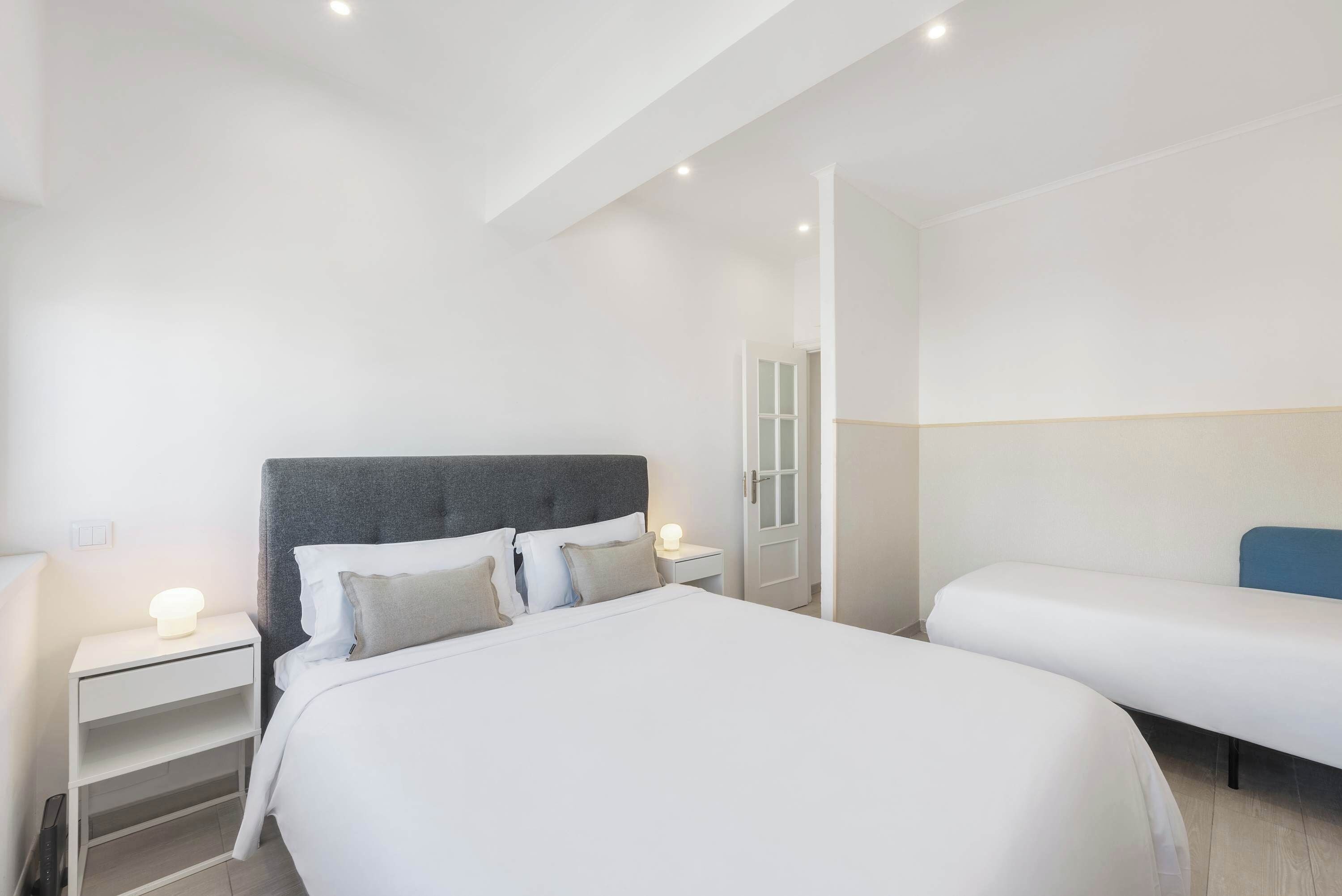 Una habitación de hotel moderna con una cama grande, una mesita de noche con lámpara y una zona de descanso separada.